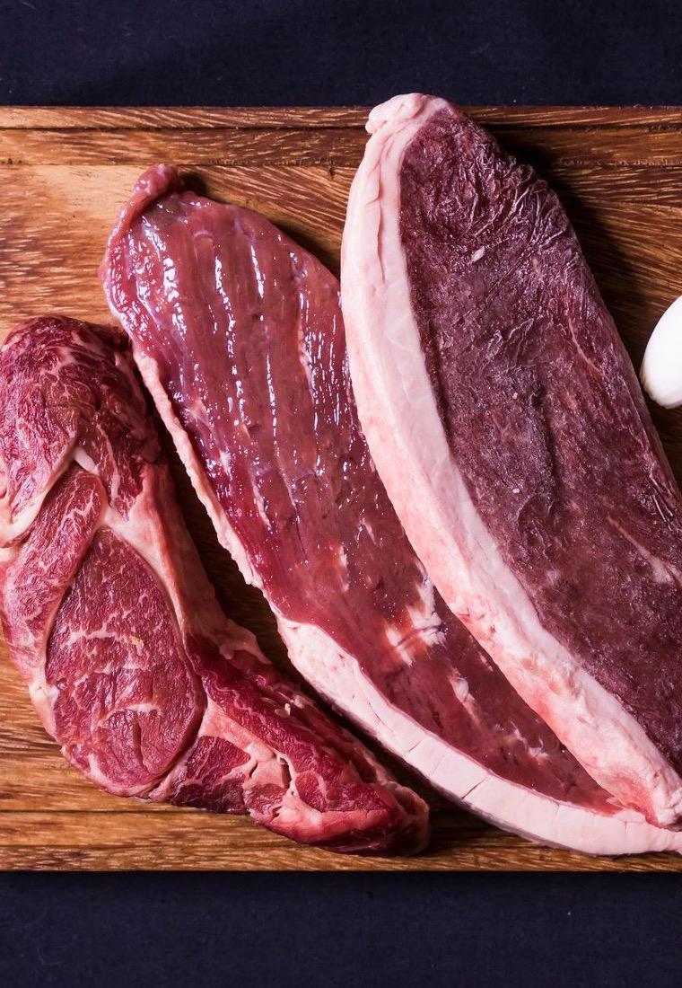 Raw meat and vegetables laid out on a wooden board